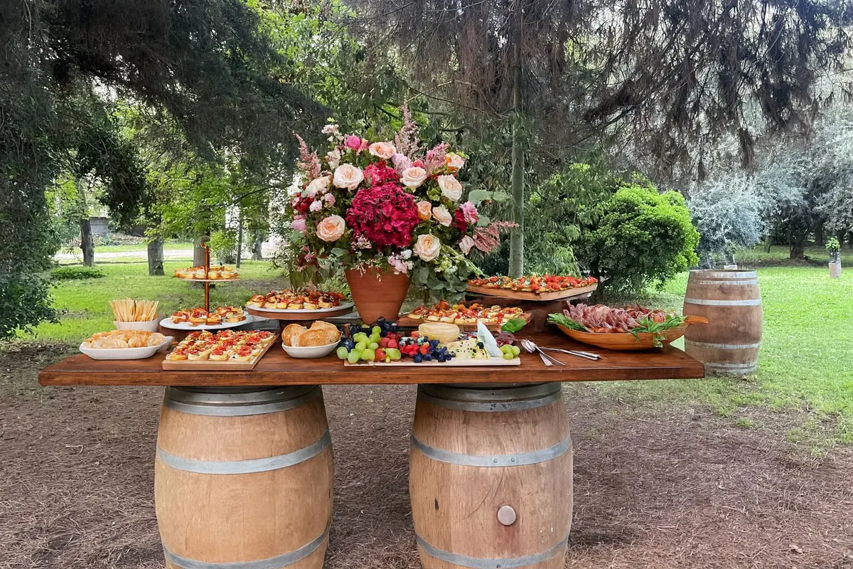 Mesa de cóctel sobre barricas decorada con flores y alimentos